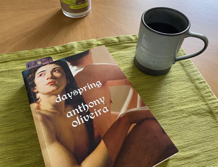 Dayspring Dayspring book by Anthony Oliveira sitting on a table next to a coffee mug.